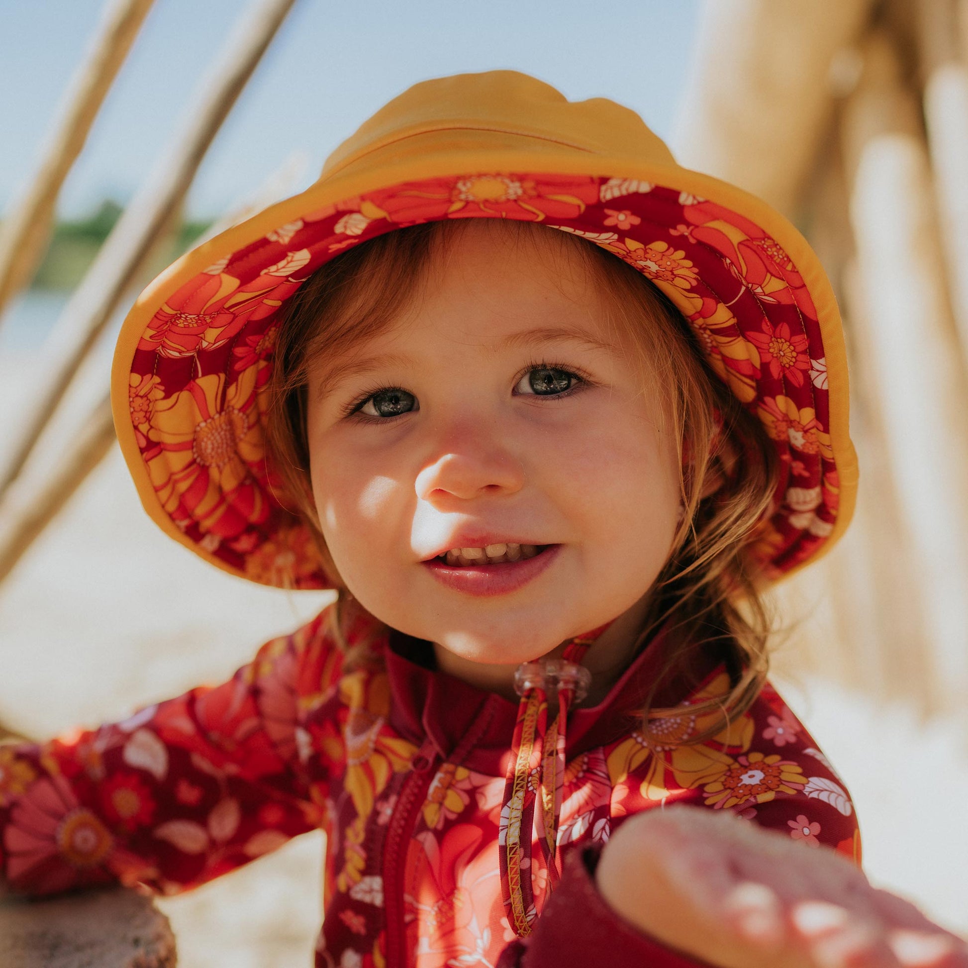 Toddler wearing Pipi Swimwear floral full length sunsuit and matching reversible wide brim swim hat