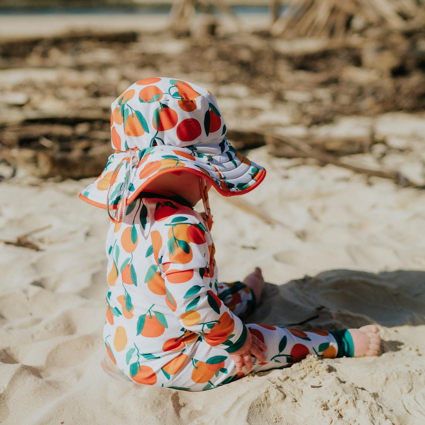 Baby wearing Pipi Swimwear mandarin fruit full length sunsuit and matching reversible wide brim swim hat
