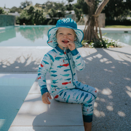 Toddler wearing Pipi Swimwear narwhal full length sunsuit and matching wide brim reversible swim hat
