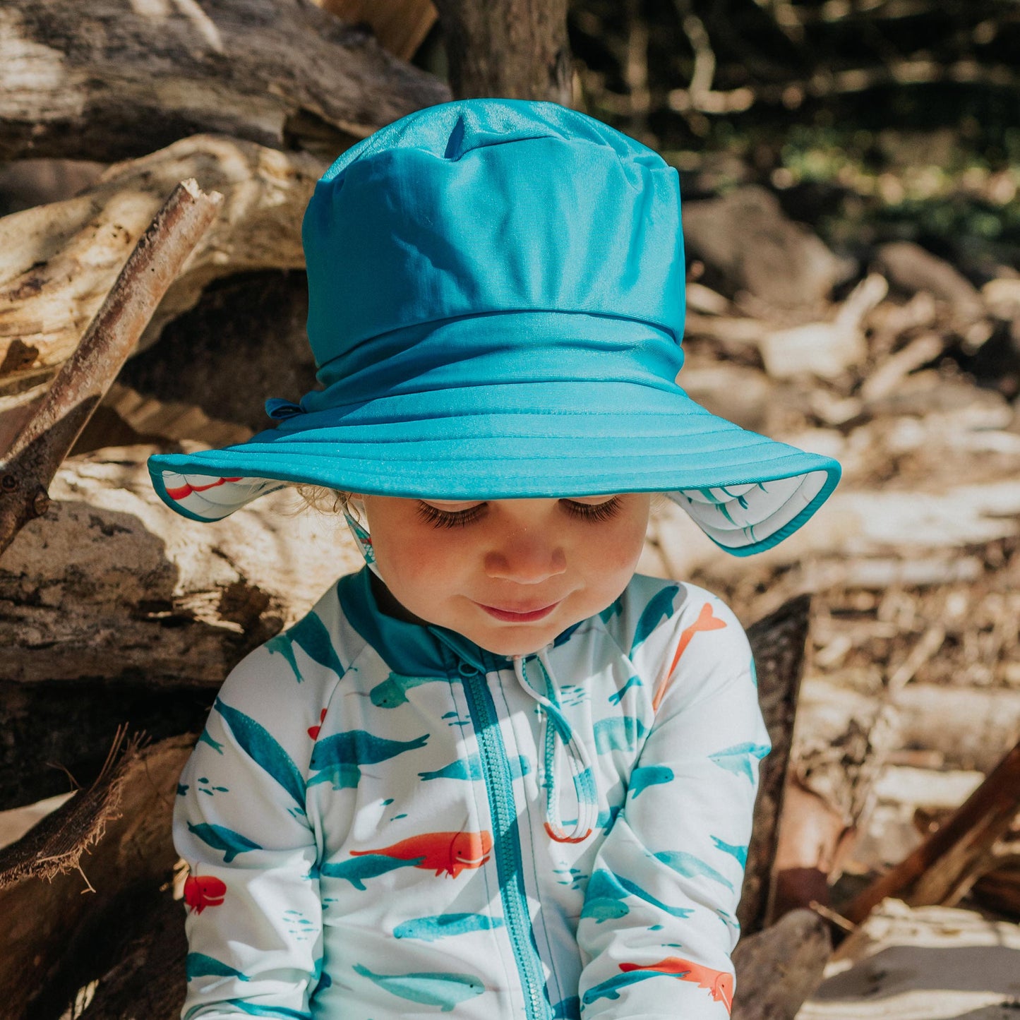 Toddler wearing Pipi Swimwear narwhal full length sunsuit and matching block colour wide brim reversible swim hat