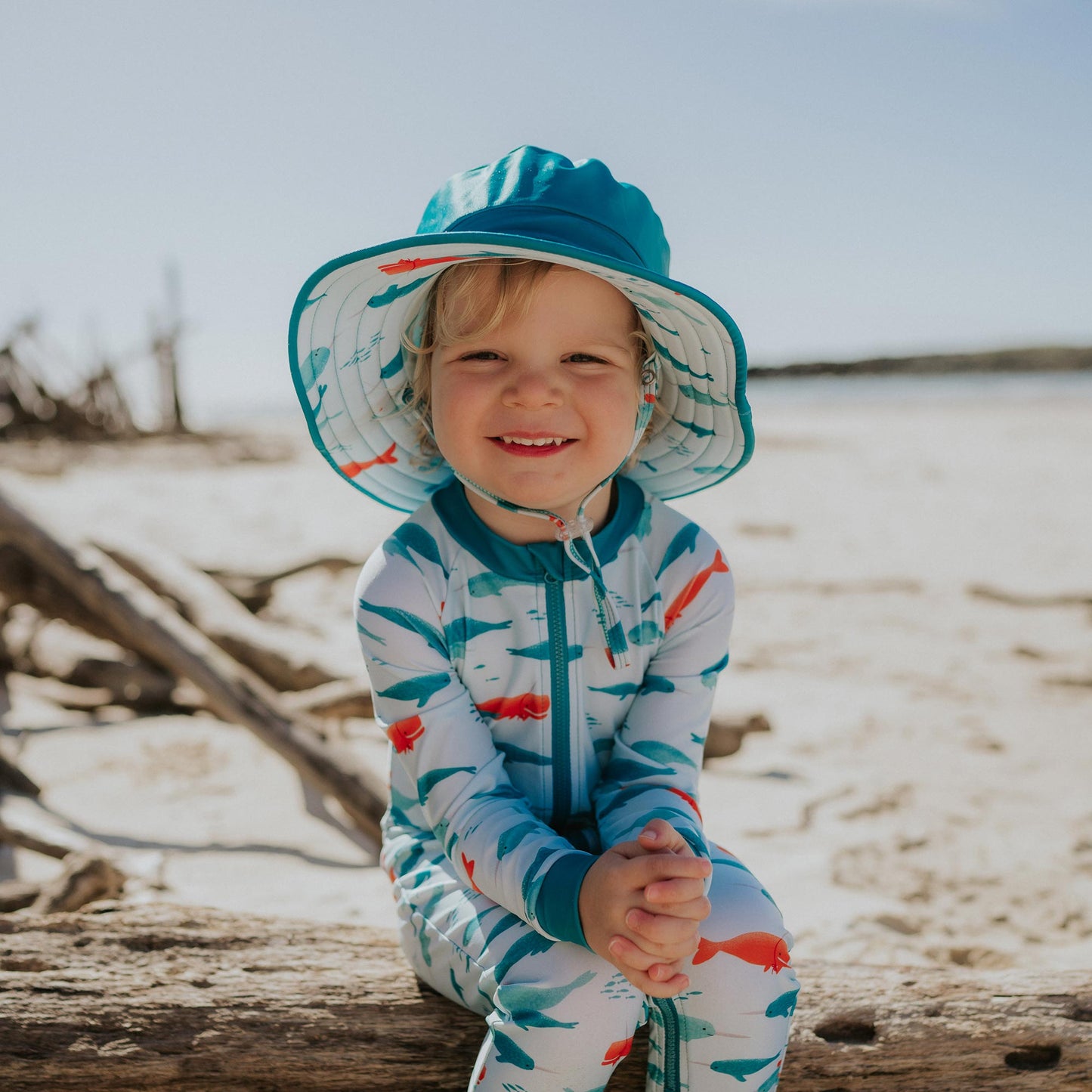 Toddler wearing Pipi Swimwear narwhal full length sunsuit and matching wide brim reversible swim hat